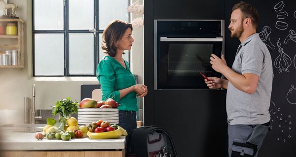 Technician talks to a woman in a kitchen with appliances. 
