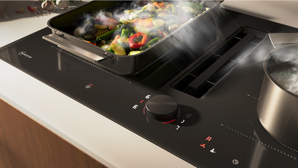 Vista di un piano cottura con cappa integrata in fase di aspirazione automatica del vapore che fuoriesce da una pentola in cui vengono cucinati degli asparagi