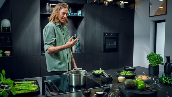 Een man staat in een moderne, donkere keuken voor een kookplaat met afzuiging en houdt een Twist Pad Flex in zijn hand