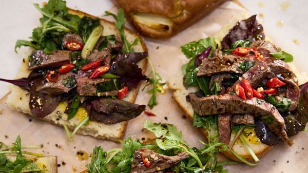 Twee open-faced sandwiches belegd met gesneden rundvlees, gemengde groenten, pepers en een drupje saus, geserveerd op knapperig brood. 