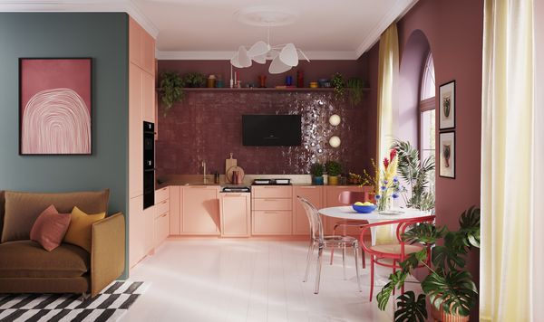 Una cucina moderna con armadietti rosa tenue, un tavolo bianco, decorazioni colorate, piante in vaso e un'area salotto accogliente con opere d'arte vivaci.