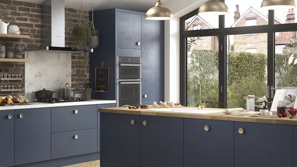 Cucina con isola centrale blu, piano in legno, elettrodomestici integrati e finestre che illuminano l&rsquo;ambiente