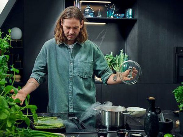 Man in black kitchen, opening pot, steam is getting drawn into venting cooktop 