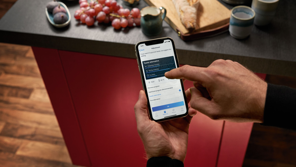 Een persoon houdt een smartphone vast met daarop de NEFF Home Connect-app en Smart Start-functie voor zijn vaatwasser