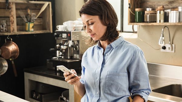 Eine weibliche Person steht in der Küche und schaut auf ihr Smartphone