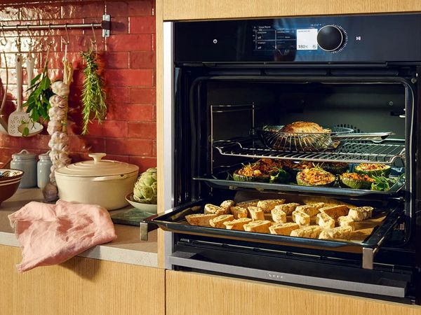 Open Slide & Hide oven showing 3 trays of food in a fully equipped kitchen.