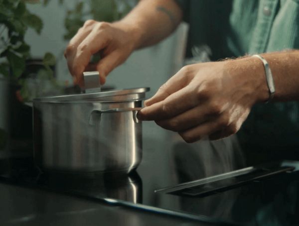 Person's hands adjusting the lid of a steaming pot on a modern stovetop with greenery nearby.