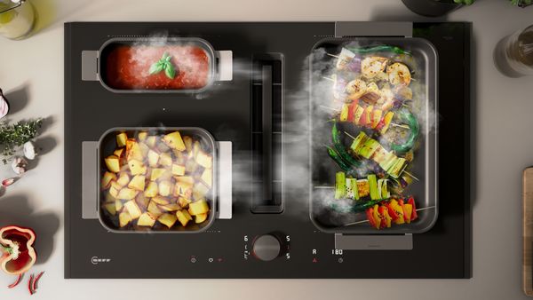 Beeld van een kookplaat met afzuiging, met daarop een pan met tomatensaus, een pan met gebakken aardappelen en en een teppanyaki met kleurrijke spiesen.