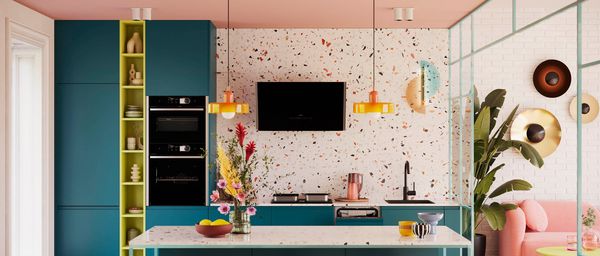 Eine lebendige K&uuml;che mit t&uuml;rkisfarbenen Schr&auml;nken, einer Terrazzo-Wand, bunten Pendelleuchten und floraler Dekoration auf einer K&uuml;cheninsel aus Marmor. 