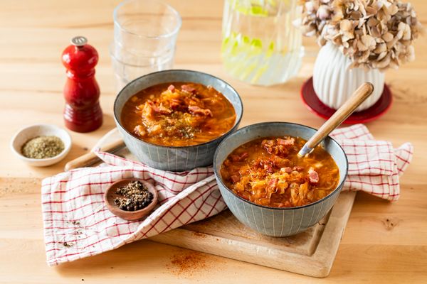 Due ciotole di zuppa calda su tagliere di legno, con spezie e tovagliolo a quadri