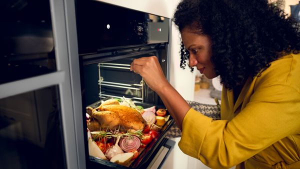 Woman checking on Thanksgiving turkey in oven.