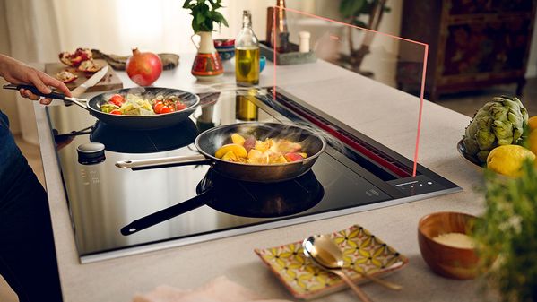 Glass draft hood shown with various dishes cooking on hob