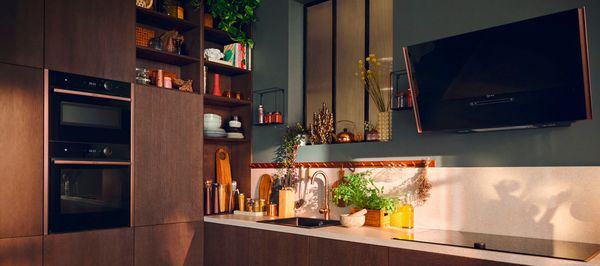 Moderni juoda virtuvė su elegantiškais prietaisais, šviečiančiu langu ir maisto ruošimo garais - stilinga kulinarinė aplinka.