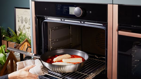 Transferring a pan of cod in tomato sauce into the oven for baking