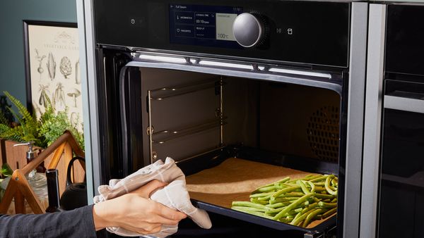 Transferring a baking tray with green beans into the oven for baking