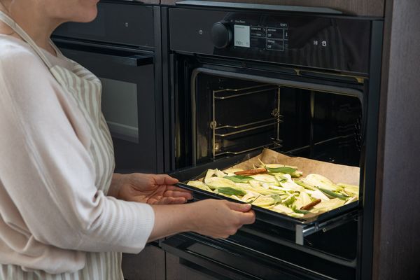 Donna in cucina inforna verdure su teglia con carta forno