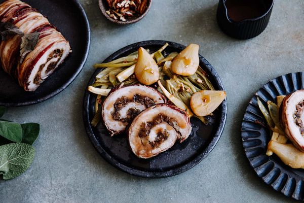 Een spiraalvormige schotel van varkensvlees overgoten met kruiden, geserveerd met geroosterde peren en groene  