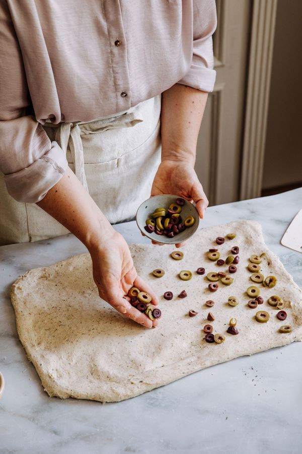 Olives sprinkled over the dough which is laid flat over the kitchen surface. 