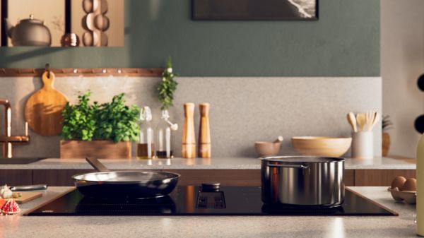 Modern kitchen with cooking pots on a sleek induction stovetop and fresh herbs on the counter. 