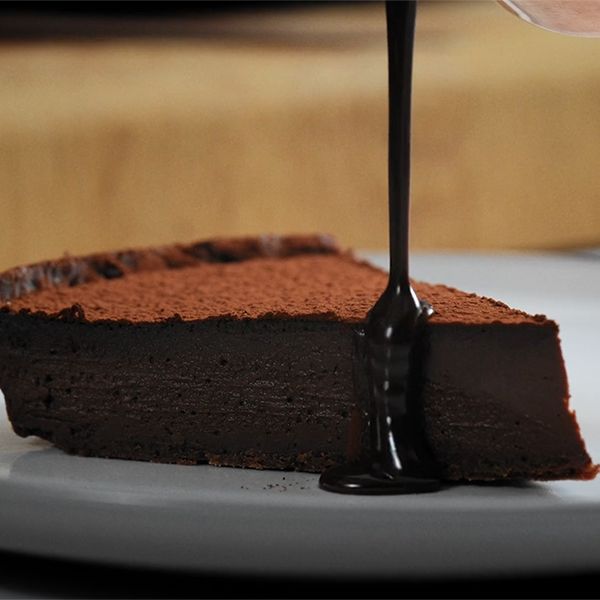 A slice of dark chocolate tart on a plate with sauce being drizzled on top