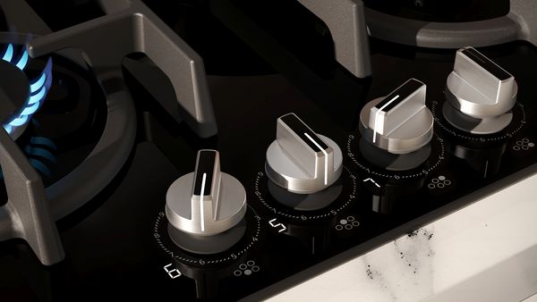 Primo piano di un piano cottura moderno con eleganti manopole in metallo e un bruciatore acceso.