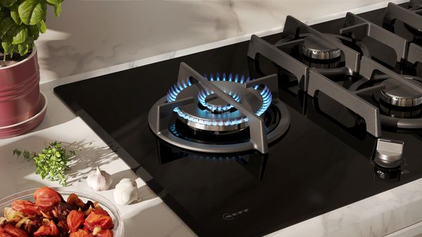 Piano cottura a gas con bruciatore acceso e fiamme blu, circondato da spezie fresche e una ciotola.