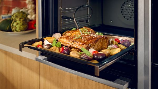 A large oven with a tray of food inside, featuring a meat probe for monitoring cooking temperature.  