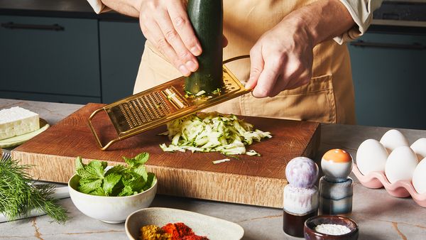 Grating a zucchini with a golden grater on a wooden board