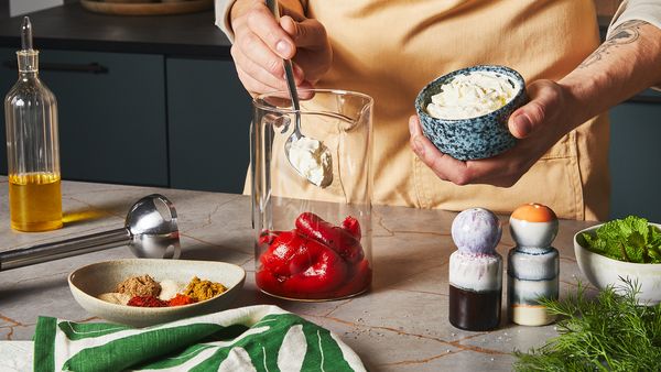 Spooning yogurt into a glass jar filled with roasted red bell peppers