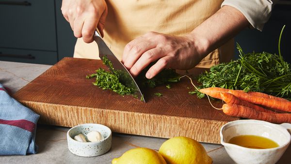 Finely cutting carrot tops on a wooden board