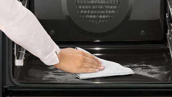 Person wiping bottom shelf of oven