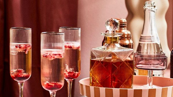 A festive bar setup with champagne flutes filled with pink drinks and berries, a crystal decanter, and a bottle of champagne on a striped tray.