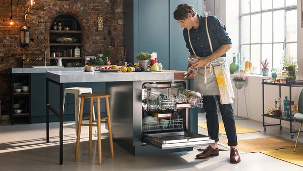 A man stands in front of an open dishwasher, preparing to load or unload dishes. 