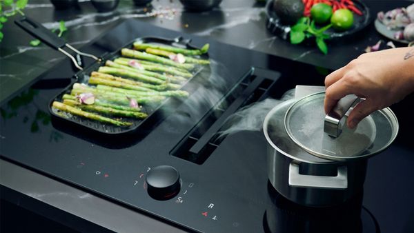 A person cooks fresh asparagus on a stovetop, showcasing vibrant green vegetables in a kitchen setting.