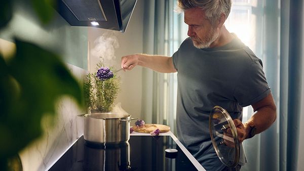 A man cooks on a stove, stirring a pot filled with fresh herbs, showcasing culinary skills and vibrant ingredients.