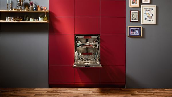 A vibrant red kitchen featuring a modern dishwasher and a neatly organized shelf for storage and display. 