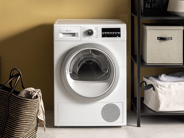 A white washing machine beside two baskets, one empty and one filled with laundry, in a bright laundry room setting.