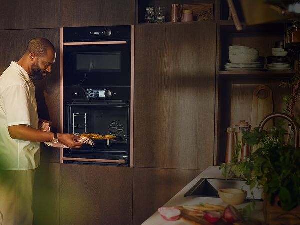 A man carefully places a dish into an oven, preparing to cook a meal. 