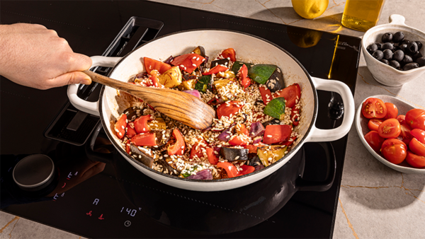 A person stirring a pot of food on a stove, with a frying sensor monitoring the cooking process.