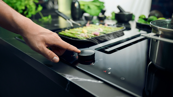 A person interacts with a touch screen on a modern stove top, demonstrating advanced cooking technology.