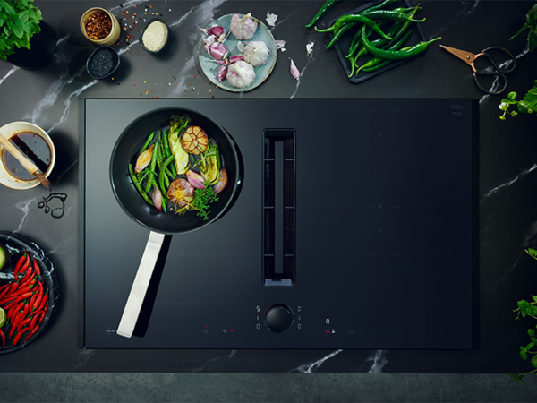 A pan filled with colorful vegetables and ingredients, placed on a venting hob, ready for cooking.