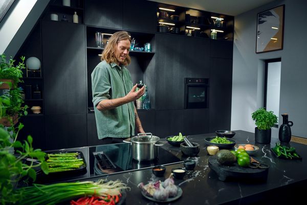 Person in a kitchen with various ingredients and a pot on the stove, showcasing contemporary design. 