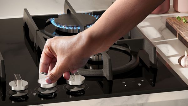 Una mano regola il livello di una manopola su un piano cottura a gas NEFF.