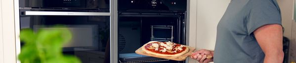 A person carefully removes a freshly baked pizza from the oven, showcasing its golden crust and melted cheese.  