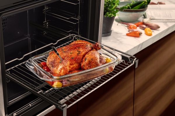 A roasted chicken with herbs and veggies on an oven rack, with a meatprobe inserted for cooking.