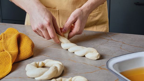 Zwei Hände verflechten zwei Teigstränge auf einer Küchenarbeitsplatte.