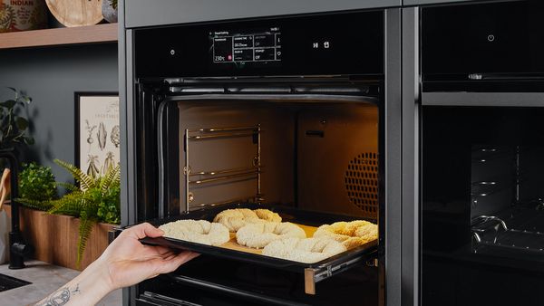 Eine Hand schiebt den zu Simits geformten Teig auf einem Backblech in den Backofen.