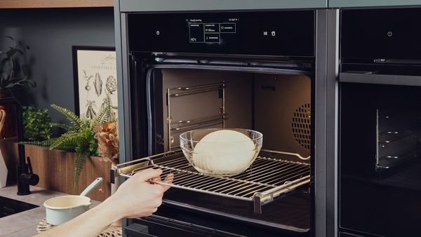 Eine Glasschüssel mit einer Teigkugel wird in den Backofen geschoben.