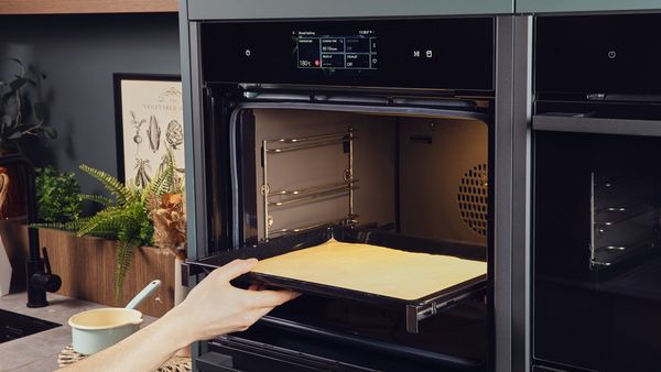 Person putting a baking tray with dough spread out on it into an oven