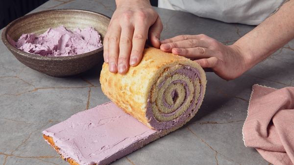 Person rolling a strip of baked dough with lilac cream in it on a kitchen countertop